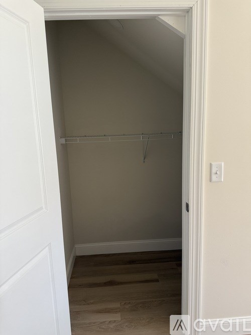 A white door is open to a small, empty room with a wooden floor.