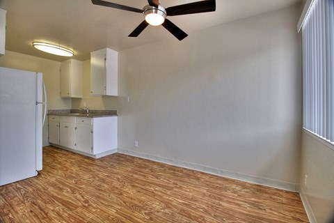 an empty living room with a kitchen and a ceiling fan