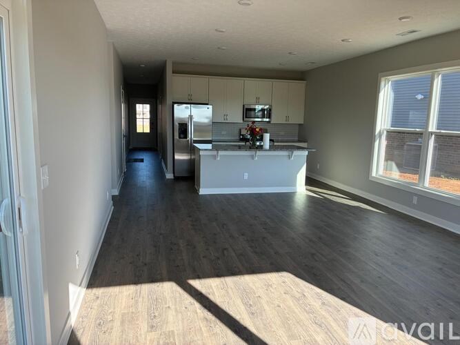 A spacious kitchen and living room with wood flooring and white cabinets.