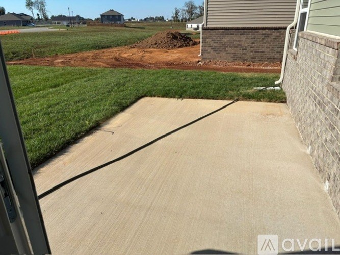 A concrete driveway leads to a house with a grassy area on the left.