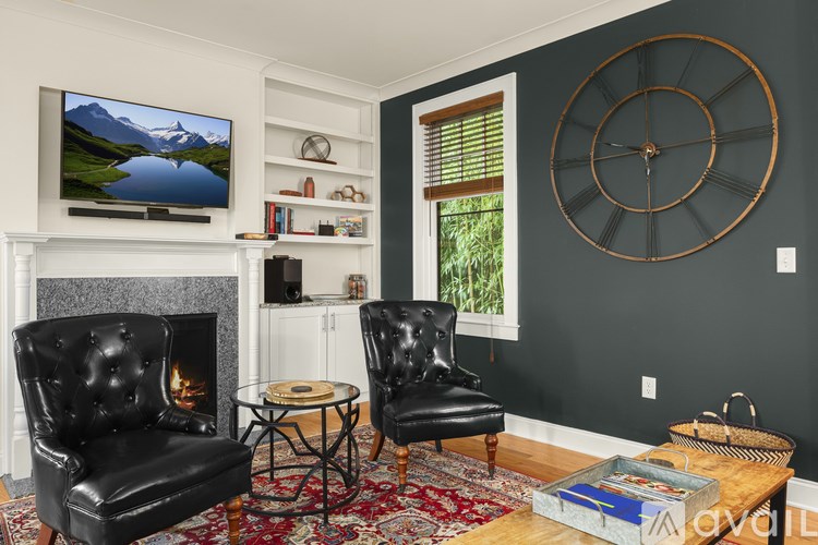 A living room with a fireplace, two chairs, a coffee table, and a large clock on the wall.