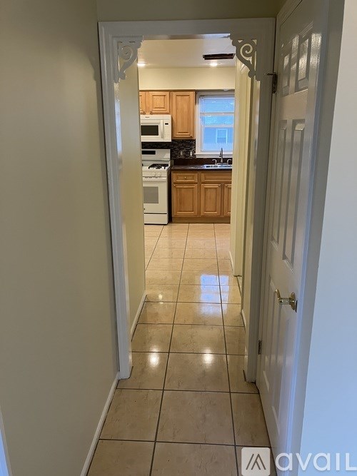 A hallway leading to a kitchen with white walls and tile flooring.