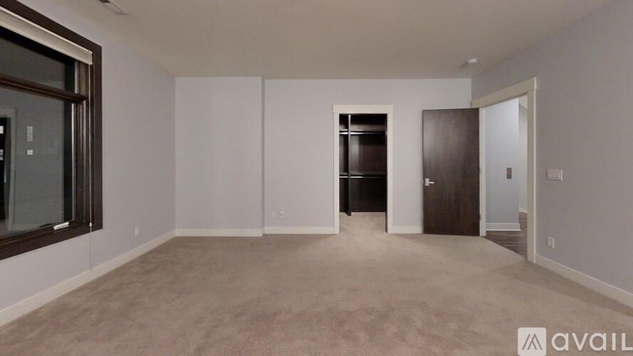 A spacious room with beige carpeting and white walls, featuring a large window, a door, and a built-in cabinet.