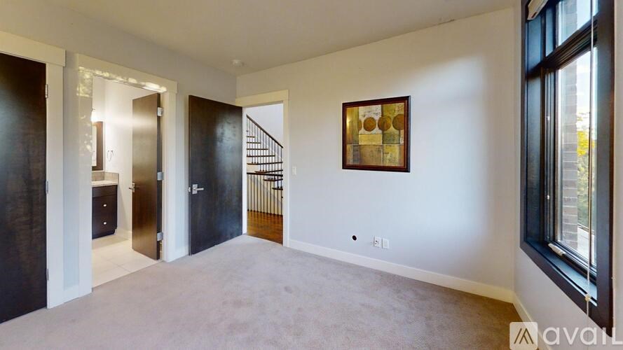 A spacious room with a carpeted floor, a staircase, and a painting on the wall.