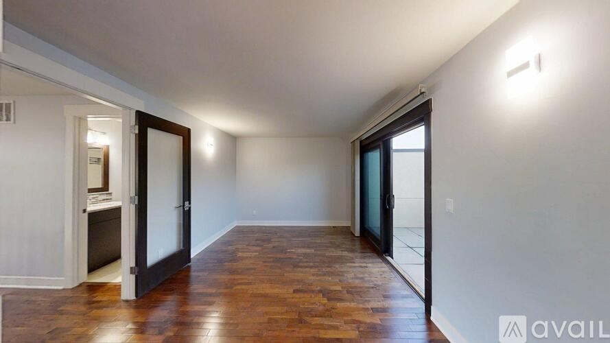 A room with wooden floors and white walls, with a door on the left and a window on the right.