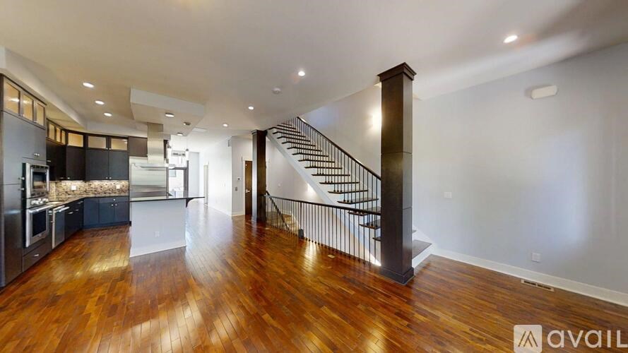 A spacious kitchen with dark wood floors and a staircase with a metal railing.