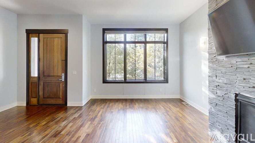 A room with a wooden floor, a door, a window, and a stone fireplace.