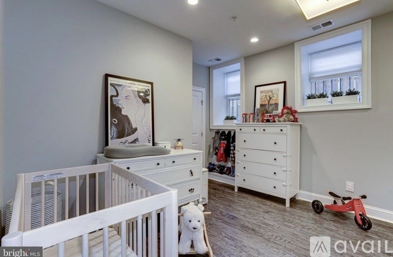 A baby's room with a white crib, a white dresser with a red toy car, and a framed picture on the wall.
