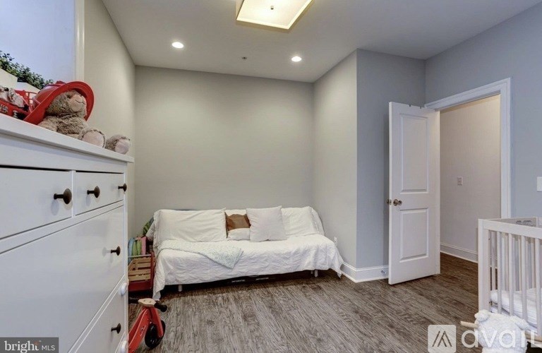 A white couch with pillows sits in a room with a white dresser and a white door.
