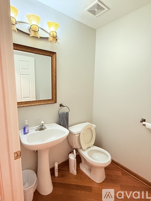 A bathroom with a toilet, sink, mirror, and light fixture.