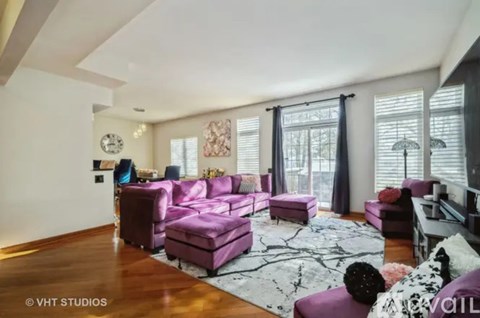 A living room with a purple couch and a white rug.