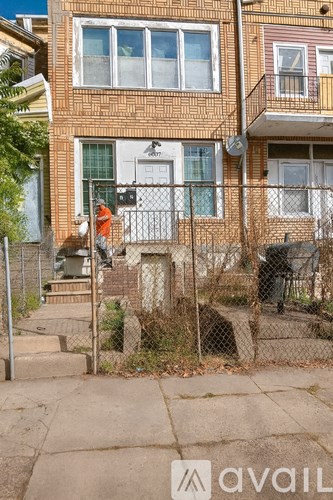 A man in an orange shirt is standing on a sidewalk in front of a brick building.