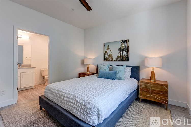A bedroom with a large bed, two lamps, and a painting on the wall.