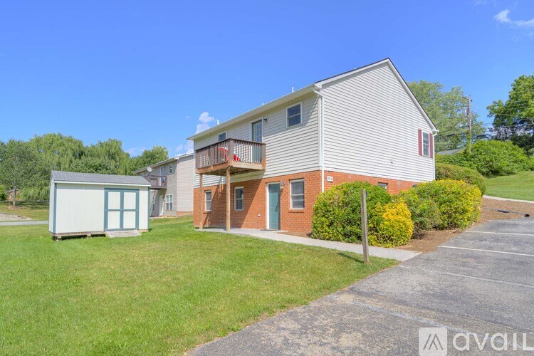 A house with a red door and a balcony is surrounded by greenery and a clear blue sky.