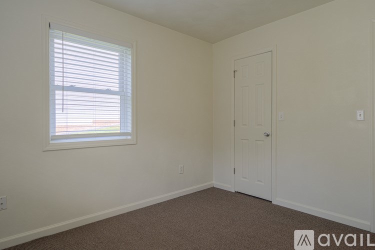 A room with a carpeted floor, a window with blinds, and a white door.
