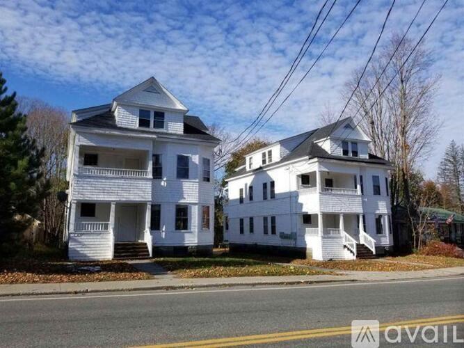 Two white houses with a road in front of them.