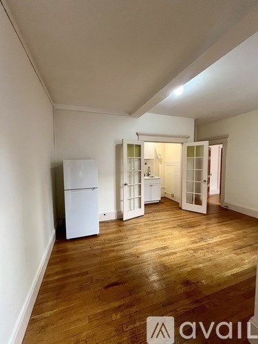 A room with a white fridge and wooden floors.
