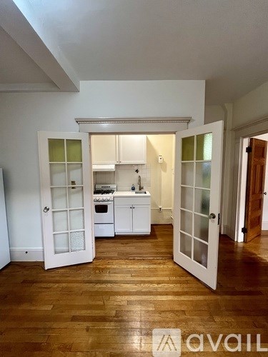 A kitchen with white cabinets and a wooden floor is open to a hallway.