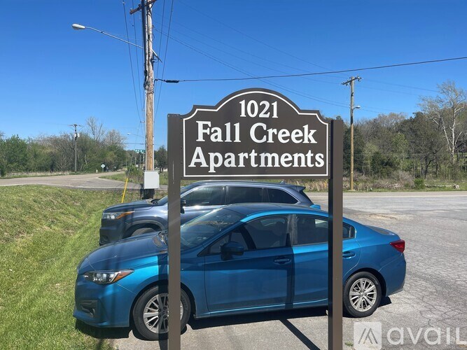 A blue car is parked in front of a sign for Fall Creek Apartments.