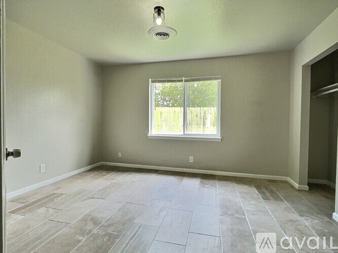 A room with a tiled floor and a window with a view of a wooden fence.