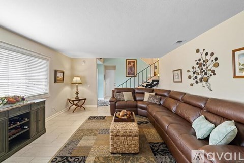 A living room with a brown leather couch and a staircase in the background.