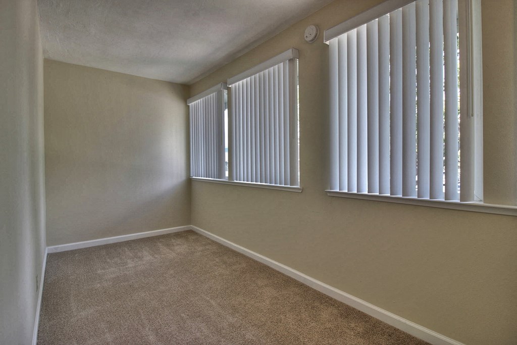 an empty bedroom with three windows with white blinds