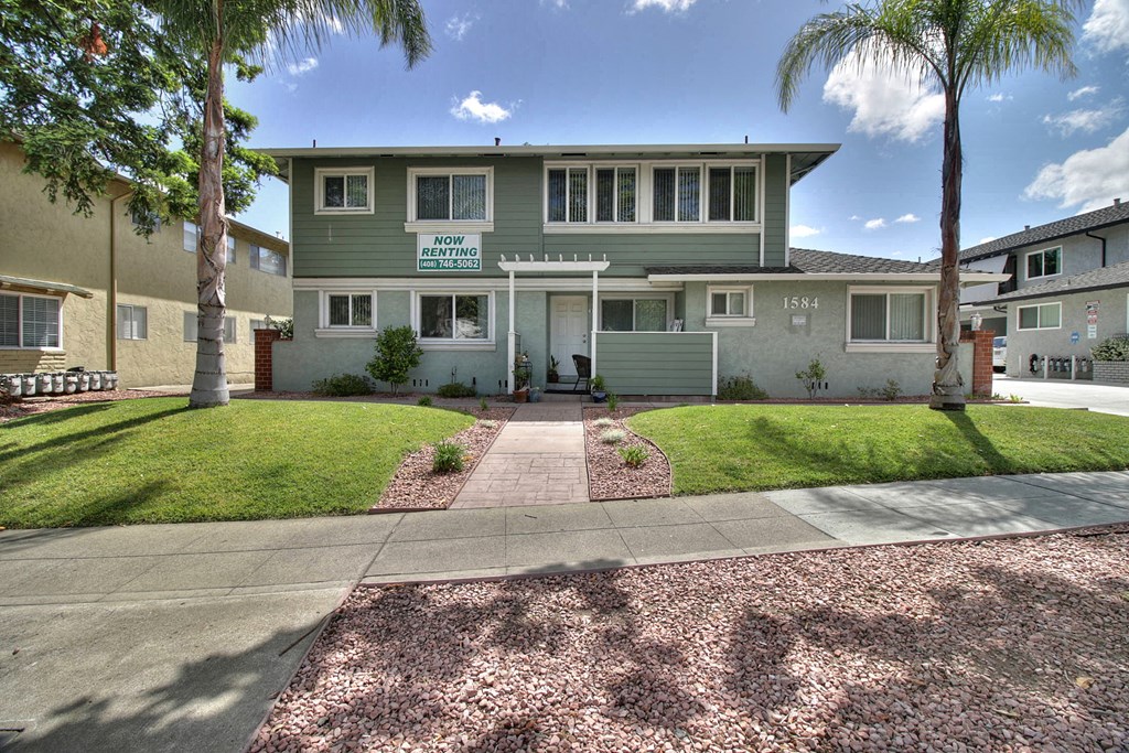 a green house with palm trees and a sidewalk in front of it
