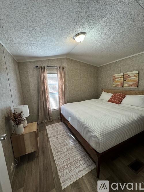 A bedroom with a bed, nightstand, and window with curtains.