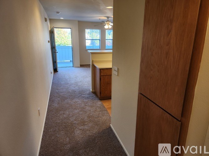 A hallway with a carpeted floor, a wooden cabinet, and a window with a view of trees and a building outside.