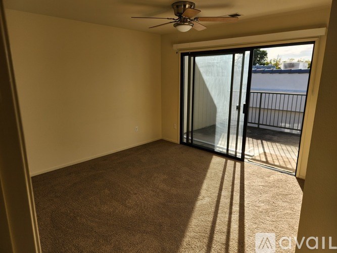 A room with a ceiling fan and sliding glass doors leading to a balcony.