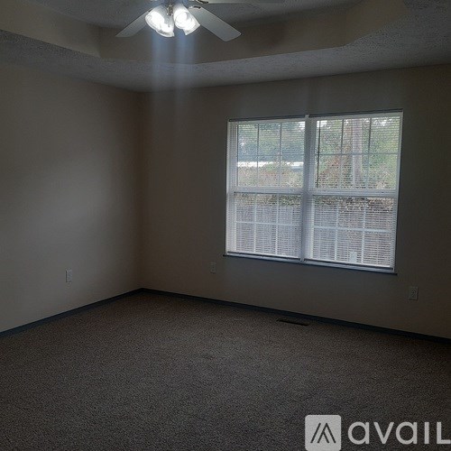 A room with a carpeted floor, a window with blinds, and a ceiling fan.
