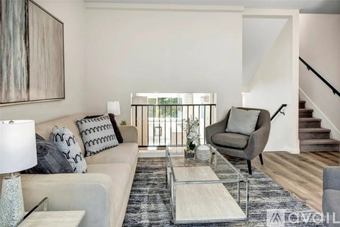 A living room with a white couch, a grey armchair, a glass coffee table, and a painting on the wall.