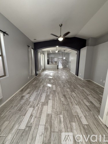 A long, empty hallway with wood flooring and a ceiling fan.