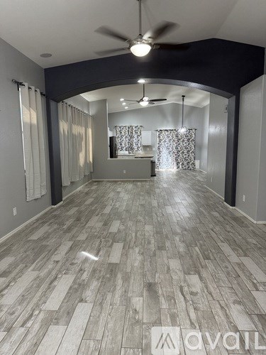A spacious room with a fan and a kitchen area in the background.