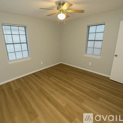 A room with wooden flooring and two windows.