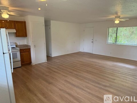 A spacious room with wooden flooring and a window with blinds.