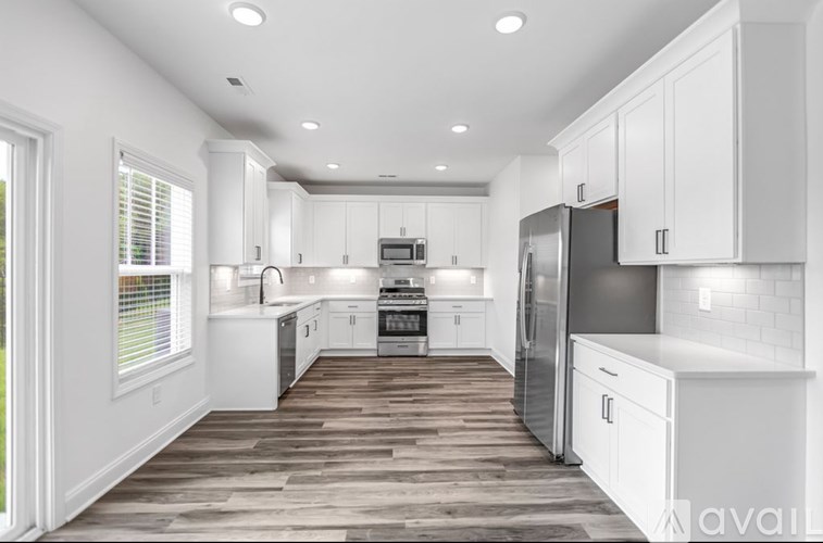 A modern kitchen with white cabinets and a wooden floor.