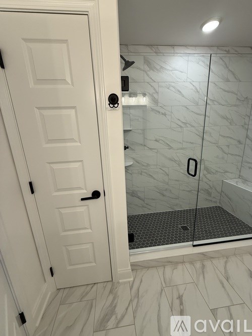 A white door with a black handle is open to a bathroom with a marble floor.