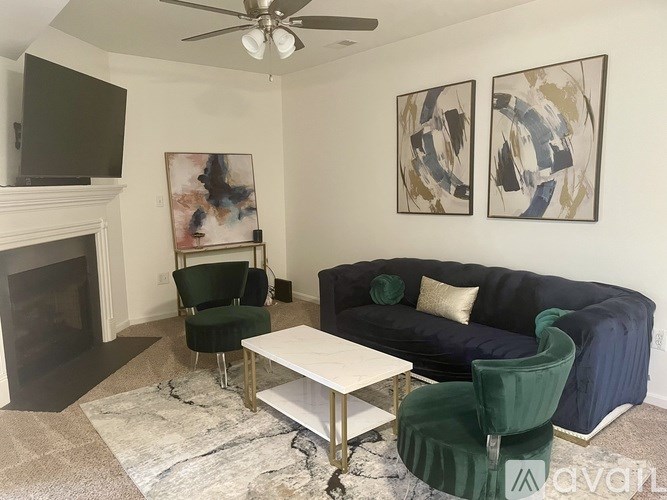 A living room with a fireplace, two chairs, a couch, and two paintings on the wall.