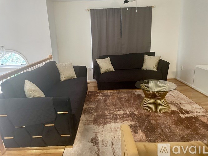 A living room with a black couch and a brown rug.