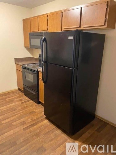 A black refrigerator in a kitchen with wooden cabinets.