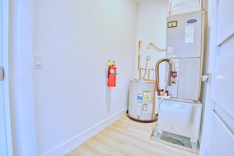 A room with a white wall and a white floor with a fridge and a fire extinguisher.
