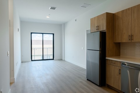 A kitchen with a refrigerator, cabinets, and a window with a view of a balcony.