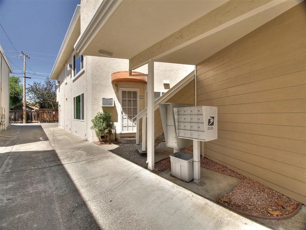 A white mailbox is on the side of a tan building.