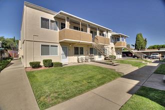 the exterior of an apartment building with a lawn and sidewalk