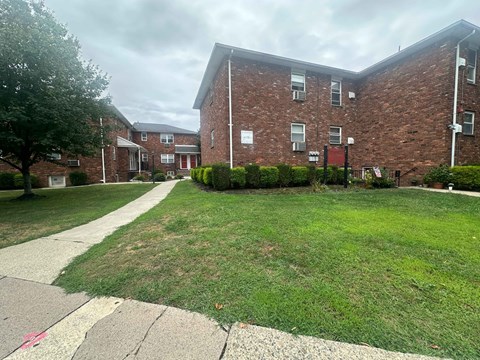A grassy area in front of a brick building with a sidewalk.