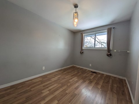 A room with wooden flooring and a window with a view of trees outside.