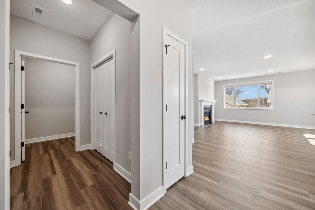 A room with white walls and wooden floors with a door on the left and a window on the right.