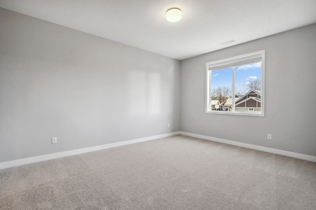 A room with a carpeted floor and a window showing a house.