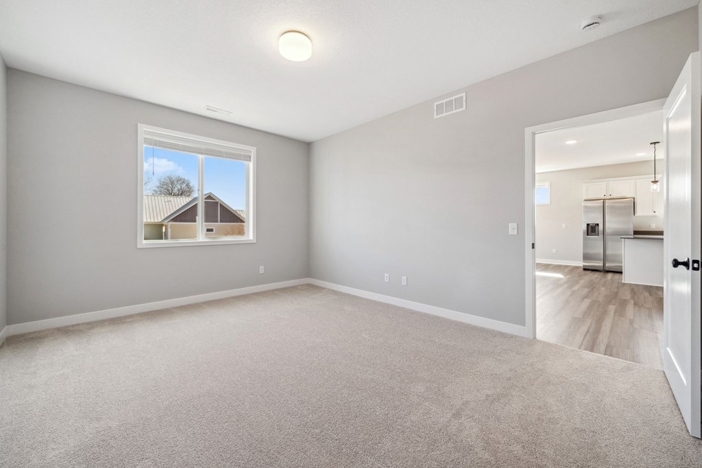 A spacious room with a carpeted floor and a window showing a house outside.